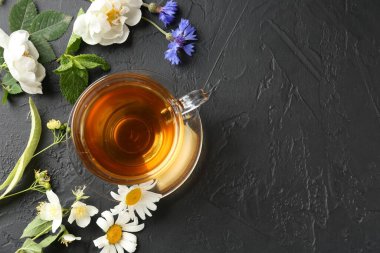 Cam fincanda aromatik bitki çayı, farklı çiçekler ve siyah masada nane şekeri. Metin için boşluk