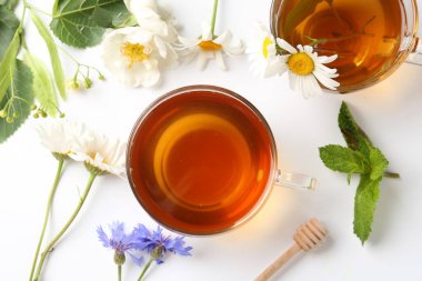 Cam fincanlarda aromatik bitki çayı, farklı çiçekler, beyaz arka planda nane ve şeker, düz uzanmış