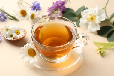 Cam fincanda aromatik bitki çayı ve bej arka planda farklı çiçekler, yakın plan.