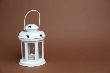 Kahverengi zemin üzerinde yanan mum ile güzel beyaz dekoratif fener, metin için boşluk