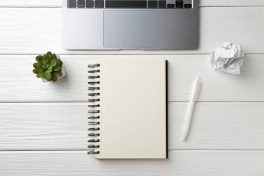 Not defteri, kalem, dizüstü bilgisayar, buruşmuş kağıt ve beyaz ahşap masa üzerindeki çiçek dekoru, düz yatış.