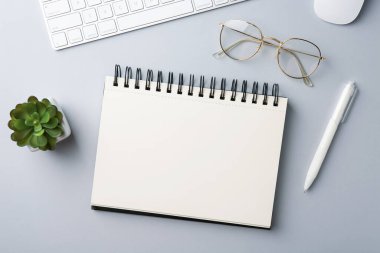 Not defteri, kalem, gözlük, bilgisayar klavyesi, fare ve çiçek dekoru gri arka planda, düz konum