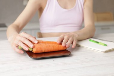 Mutfak terazisinde havuç tartan kadın. Beyaz ahşap masa, yakın plan.