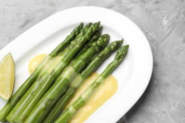 Sos ve limonla servis edilen lezzetli pişmiş kuşkonmaz. Gri desenli masa, yakın plan.