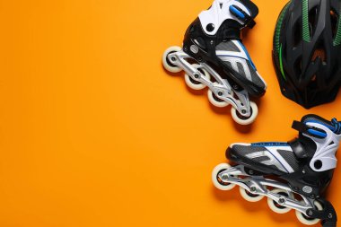Turuncu arka planda bir çift paten ve kask, üst manzara. Metin için boşluk