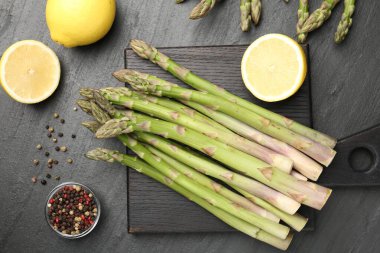 Taze çiğ kuşkonmaz mızrakları, limon ve baharatlar siyah masada, düz yerde.