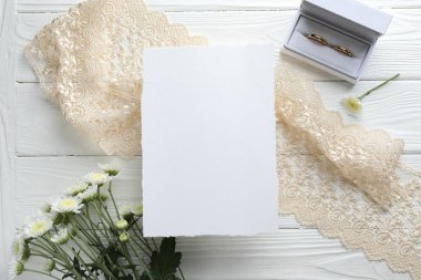 Düğün davetiyesi, altın yüzükler ve çiçekler beyaz ahşap masada, düz yatıyordu.