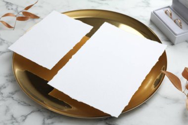 Düğün davetiyeleri, altın tepsi, yüzükler ve dallar beyaz mermer masa üzerinde kuru yapraklar, yakın plan