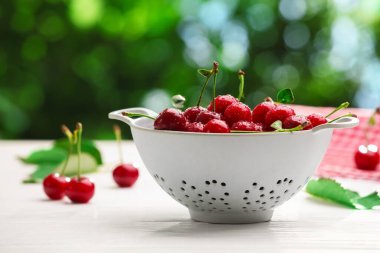 Taze ıslak kirazlar beyaz ahşap masada, bulanık yeşil arka planda, yakın plan.