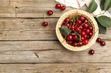 Hasır sepetin içinde taze ıslak kirazlar ve ahşap masanın üzerinde düz yapraklar. Metin için boşluk