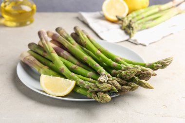 Açık gri masada taze çiğ kuşkonmaz ve limon, yakın plan.