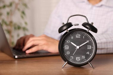 Son teslim tarihi. Çalar saat ve adam tahta masada dizüstü bilgisayarda çalışıyor, seçici odaklanma