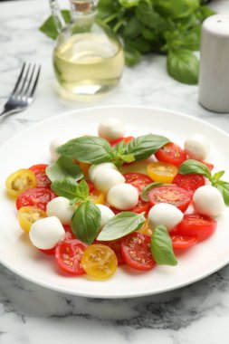 Mozarella soslu lezzetli salata, domates ve fesleğen beyaz mermer masada, yakın plan.