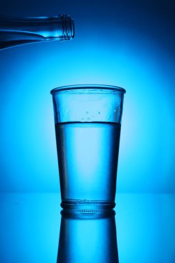 Mavi arkaplanda, tatlı su bardağının üstünde bir şişe. Arka ışıklandırma