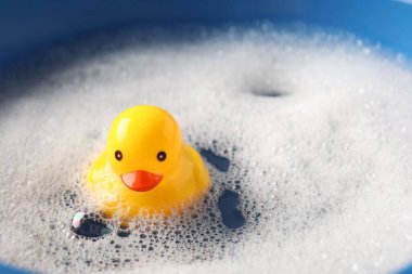 Mavi arka planda köpüklerle suda yüzen sevimli plastik ördek, yakın plan.