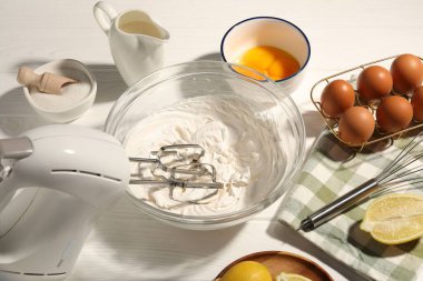 Beyaz ahşap masada çırpılmış krema, yumurta ve diğer ürünlerle karıştırıcı.