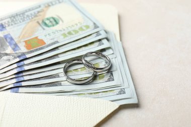 İki gümüş alyans, dolar banknotları ve beyaz masanın üzerindeki zarf, yakın plan. Metin için boşluk