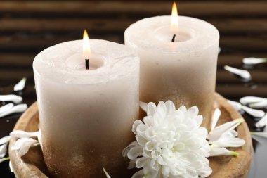 Islak siyah ayna yüzeyinde yanan mumlar ve güzel çiçekler, yakın plan.