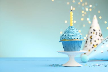 Kekin içinde yanan mum, serpiştirmeler ve açık mavi masada parti şapkaları bulanık ışıklı turkuaz arka plan, metin için yer