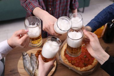 Arkadaşlar ahşap masada bira bardaklarını tokuşturur, yakın plan