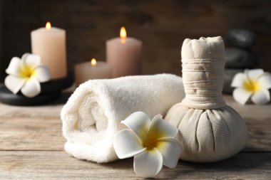 Ahşap masada bitkisel çanta, havlu ve spa taşlarıyla kompozisyon, yakın plan.