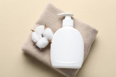 Bir şişe sıvı sabun, pamuk çiçeği ve bej arka planda havlu, üst manzara.