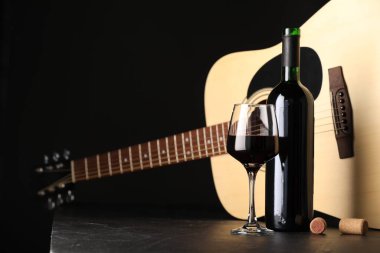 Akustik gitar ve kırmızı şarap siyah masada, yakın plan.