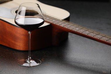 Akustik gitar ve kırmızı şarap siyah masada, yakın plan.