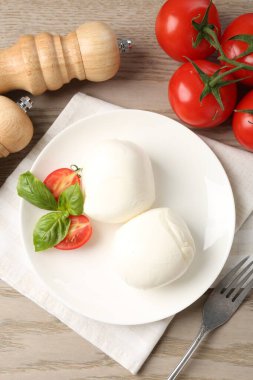 Lezzetli mozzarella peyniri topları, domates ve fesleğen ahşap masada, düz yerde.