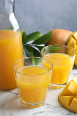 Bardakta lezzetli mango suyu, taze meyve ve yeşil yapraklar beyaz mermer masada, yakın plan.