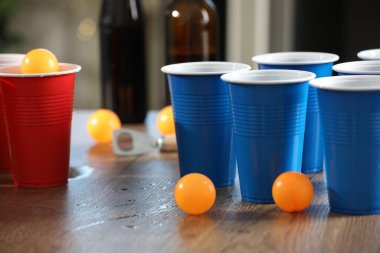 Bira pong oyunu. İçkili plastik bardaklar ve toplar ahşap masada, yakın plan.