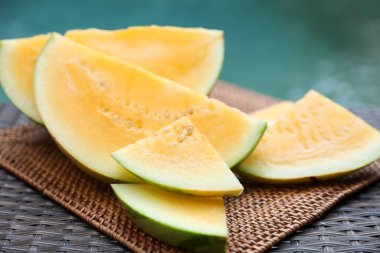 Olgun sarı karpuz parçaları hasır masada, yüzme havuzunun yanında, yakın plan.