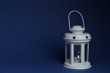 Mavi zemin üzerinde yanan mum ile güzel beyaz dekoratif fener, metin için boşluk
