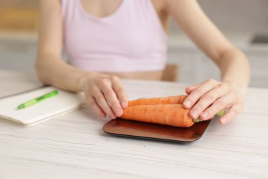 Mutfak terazisinde havuç tartan kadın. Beyaz ahşap masa, yakın plan.