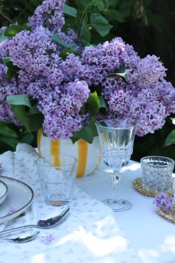 Güzel leylak çiçekleri, bardaklar, çatal bıçak takımı ve mum bahçedeki masada.