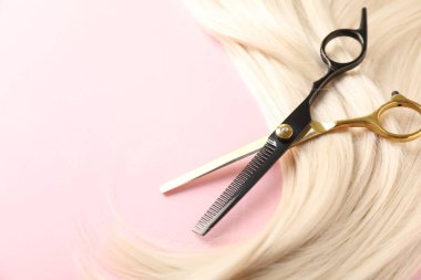 Açık pembe arka planda saç teli ve makas, yakın plan. Metin için boşluk