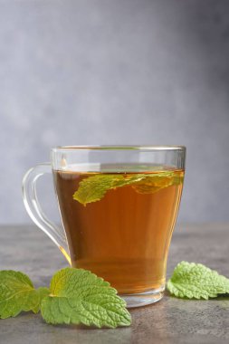 Cam bardakta Aromatik limon merhemi çayı ve gri desenli masada taze yapraklar.