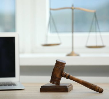 Dizüstü bilgisayar, yargıç tokmağı ve terazileri ofisteki ahşap masada.