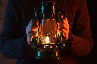 Ahşap duvarın yanında eski tip gaz lambası tutan adam, yakın plan.