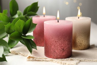 Bulanık ışıklara karşı beyaz masada yanan mumlar ve yeşil yapraklar.