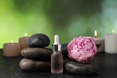 Koyu dokulu masa üzerinde taşlar, damlalar ve çiçekli spa bileşimi bulanık yeşil arkaplan, yakın plan