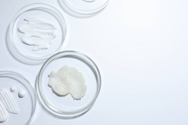 Petri kabında farklı kozmetik ürünleri, beyaz arka planda, düz yerde. Metin için boşluk
