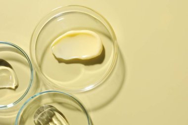 Petri kabında farklı kozmetik ürünleri, soluk sarı arka planda, düz yerde. Metin için boşluk