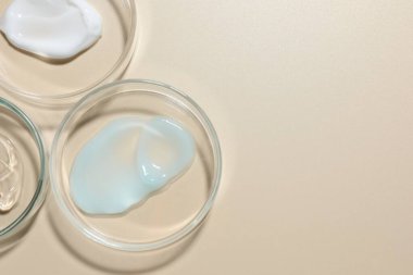 Petri kaplarında bej arka planda farklı kozmetik ürünleri var. Metin için boşluk