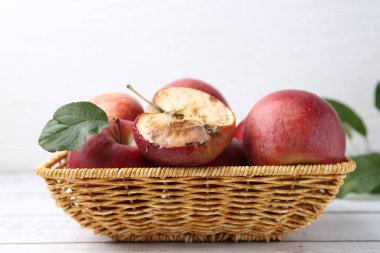 Şımarık elma ve güzel elmalar sepetin içinde, beyaz tahta masada, yakın plan.