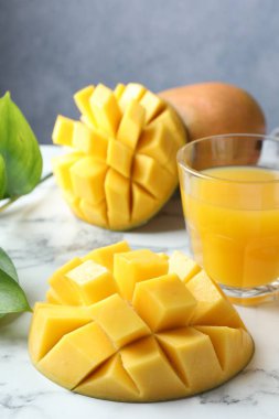 Bardakta lezzetli mango suyu, taze meyve ve yeşil yapraklar beyaz mermer masada, yakın plan.