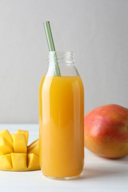 Cam şişede lezzetli mango suyu ve beyaz ahşap masada taze meyve, yakın plan.