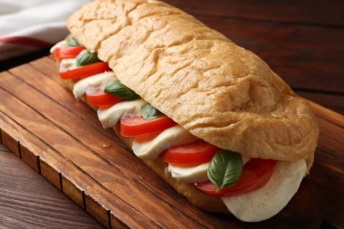 Mozarella peynirli, domatesli ve ahşap masadaki fesleğenli lezzetli sandviç.