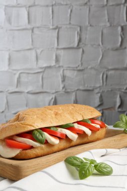 Mozarella peynirli, domatesli ve fesleğenli lezzetli sandviç gri desenli duvara karşı, yakın plan. Metin için boşluk