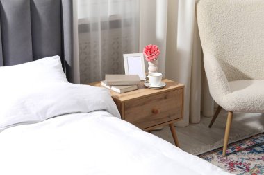 İçinde kahve, kitap ve yatağın yanında dekor olan komodin.